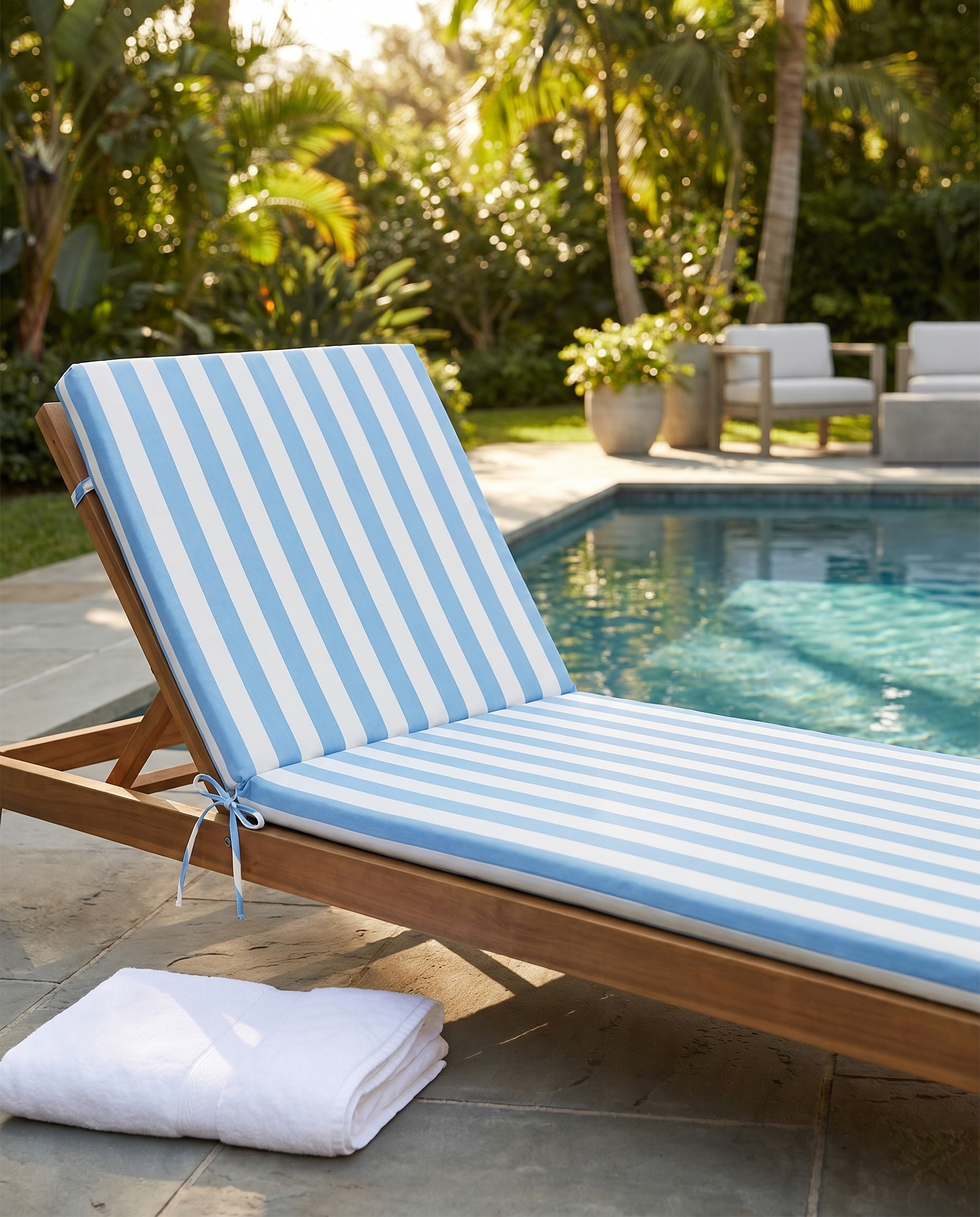 Blue and white striped chaise lounge cushion on a wooden sun lounger by a pool