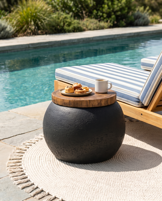 Black concrete ball side table with wood top poolside beside a lounger