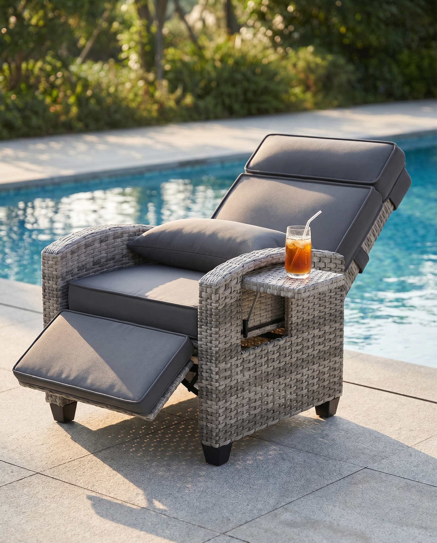 Grey rattan lay-flat patio recliner with side table beside a pool