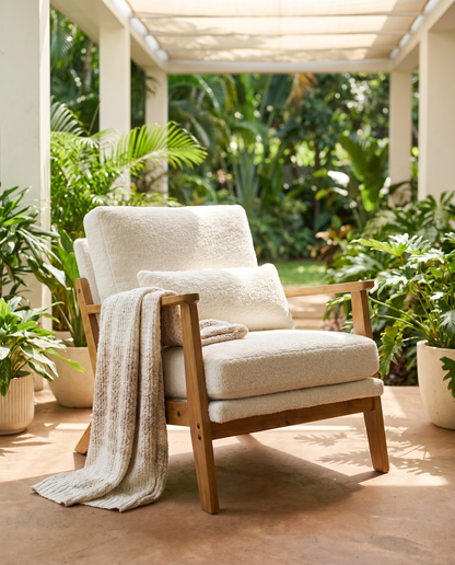 Mid-century cream boucle accent chair with wood frame on a plant-filled veranda