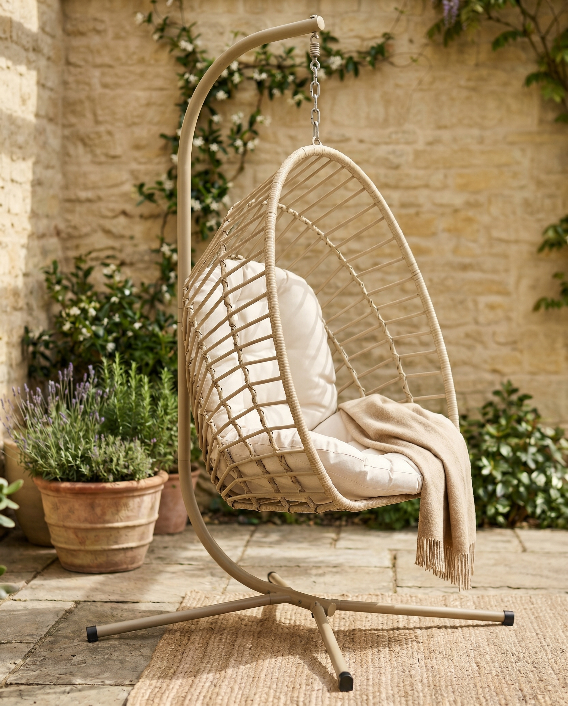 Natural rattan hanging egg chair with stand on a stone patio with lavender